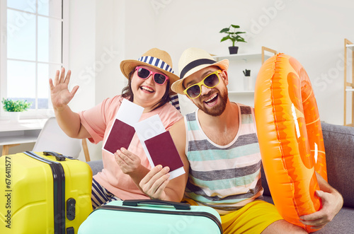 Happy family couple ready for summer vacation. Portrait funny joyful husband and wife sitting on sofa couch with rubber swim ring, holding passports and cheap tickets they purchased for holiday travel photo