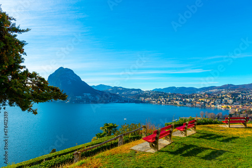 Bench and Branch and Lake Lugano and City with Mountain and Blue Sky in Park San Michele in Castagnola in Lugano, Ticino in Switzerland.