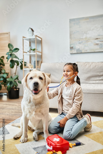 happy kid in casual attire playing doctor with labrador in modern living room, toy stethoscope