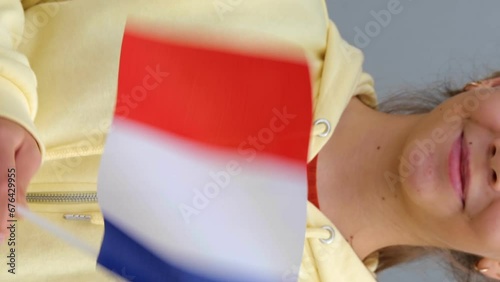 Female small girl in yellow hoodie, keeping flag of France in her hands. Beautiful Caucasian Young teenage Girl waving small French flag, smiling at camera. Real time. Vertical video. photo