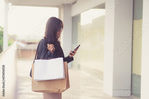 woman with shopping bags and smart phone walking near mall.