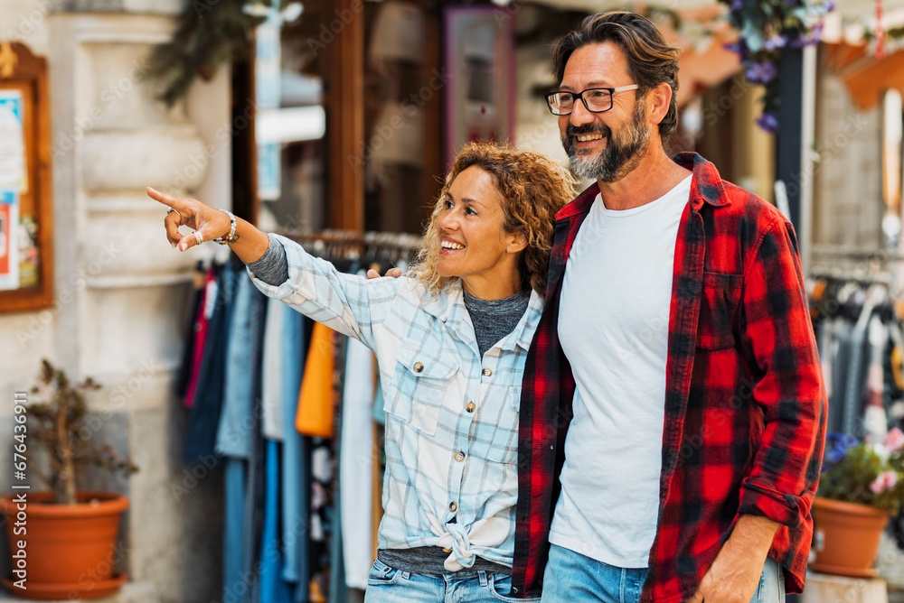 Couple of happy young adult people enjoy shopping and tourist outdoor leisure activity in the street. Man and woman enjoy walking near stores smiling and pointing in friendship relationship love