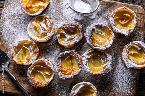 Mini tarts made of puff pastry and sliced apples sprinkled with powdered sugar on wooden cutting board