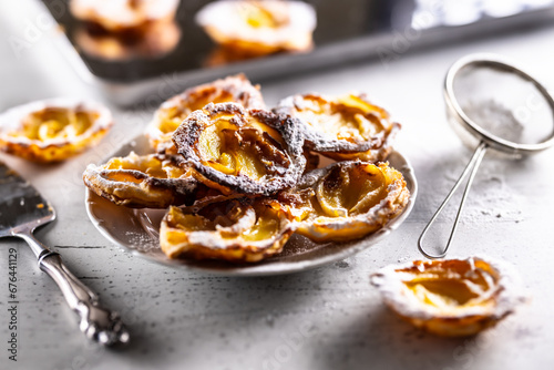 Fototapeta Naklejka Na Ścianę i Meble -  Mini tarts made of puff pastry and sliced apples sprinkled with powdered sugar on white plate