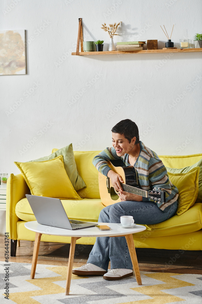 vertical shot of joyful young woman sitting on sofa with guitar looking on laptop on remote class