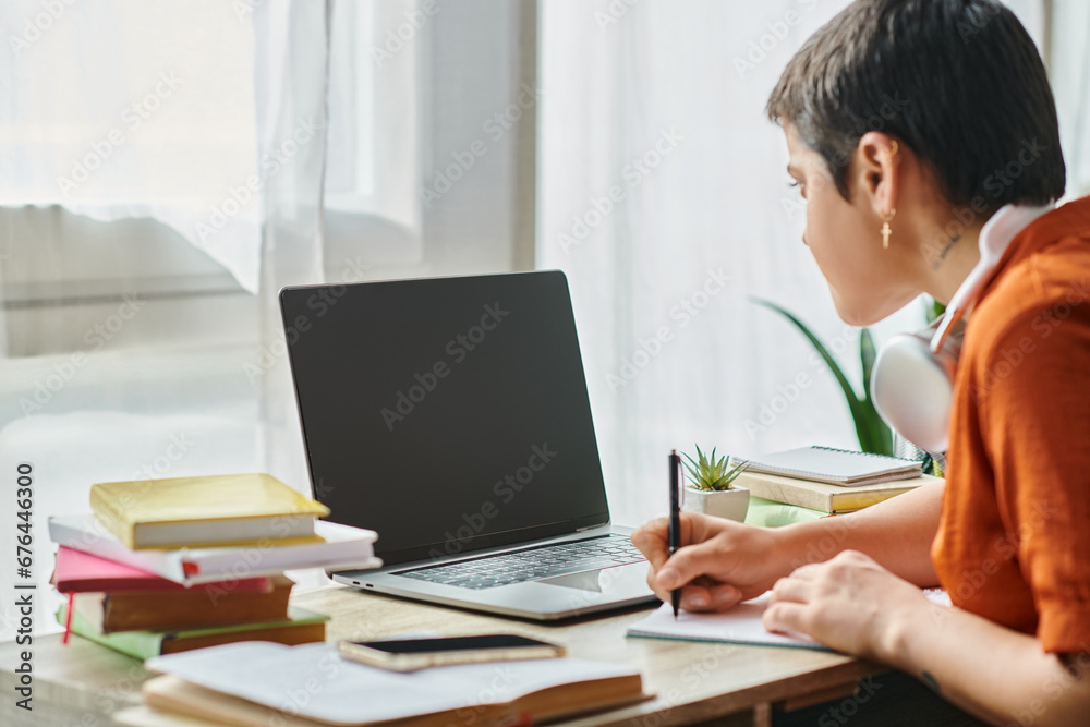 focus on laptop with blurred young student in front of it taking notes during online class focus on laptop with blurred young student in front of it taking notes during online class