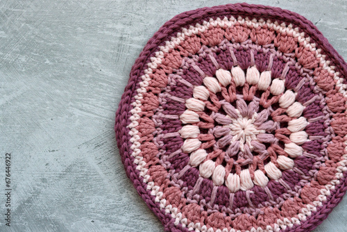 Crocheted trivet made of pink organic yarn. Handmade crochet potholder on gray background with space for text. 