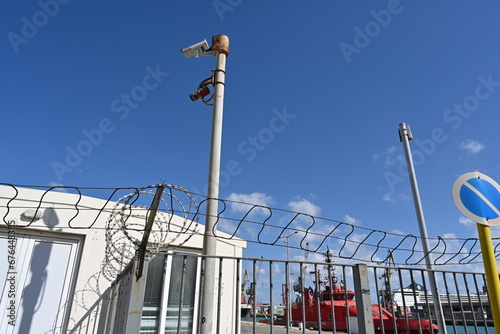 The barbed wire on top of the fence and CCTV cameras at the entrance of passenger dock. The fence protects against unauthorized entry to approach the ships. photo