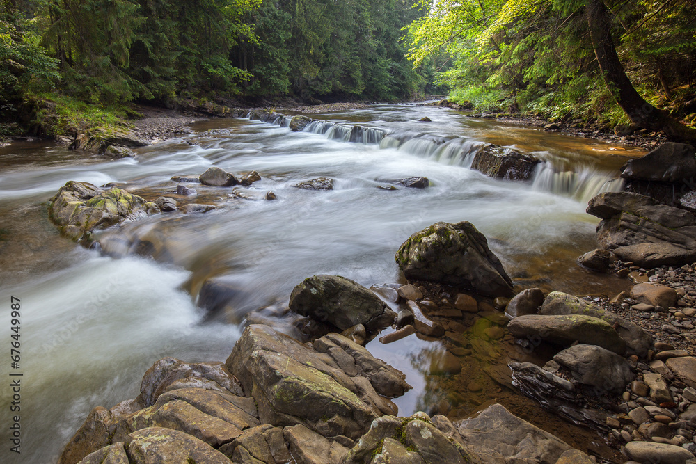 Fototapeta premium Magical raging river Candles and rapids in the mountains, in the middle of a coniferous forest, long exposure. A fabulous waterfall and a raging river with crystal clear water in the Carpathians.