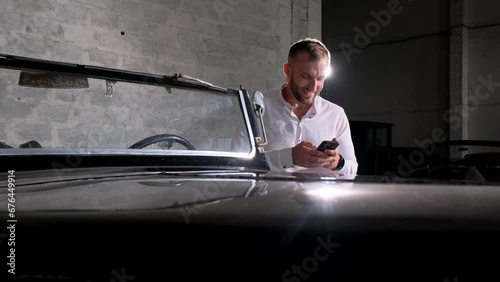 Business man holding a smartphone while standing near a retro car photo