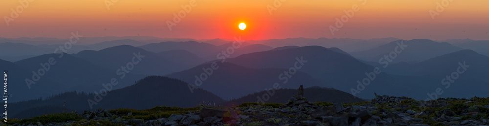 Panorama Silhouettes of Carpathian mountains in a natural blue-red gradient with the sun in the middle. Panorama of the Carpathian Mountains at dusk with silhouettes of ridges and peaks. 