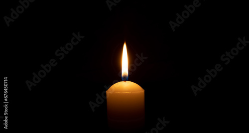 Fotografia Single burning candle flame or light glowing on a big white candle on black or dark background on table in church for Christmas, funeral or memorial service with copy space