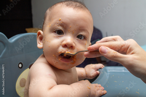 Beginning of complementary nutrition. 6 month old baby eating guava porridge. Child has fun with face full of food