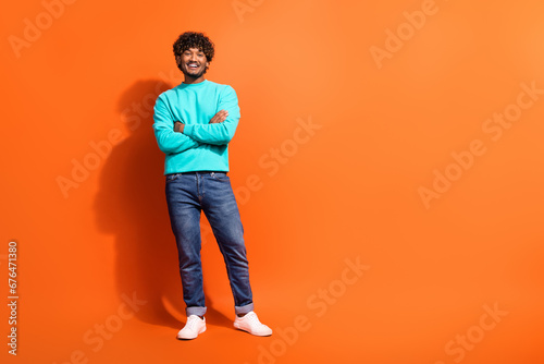 Full length body photo of young cheerful handsome indian model guy folded hands wear stylish pullover isolated on orange color background