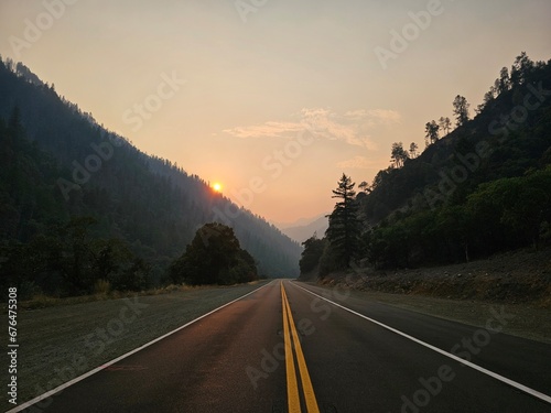 Sunset cresting the mountains of California slightly hidden by the smoking rolling in over the mountains. Highlighting a the bright paved road inviting you to the pacific ocean.