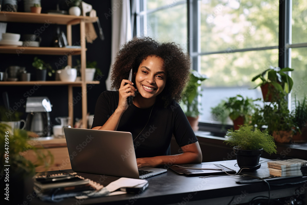 African American Female entrepreneur talking over mobile phone and looking at camera while working over laptop at home African American Female entrepreneur talking over mobile phone and looking at camera while working over laptop at home