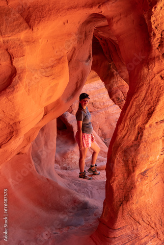 Woman standing in the fire cave and Windstone Arch in Valley of Fire State Park, Nevada, USA. Long, narrow slot canyon with sheer rock walls. Tranquil desert landscape of eroded sandstone formation