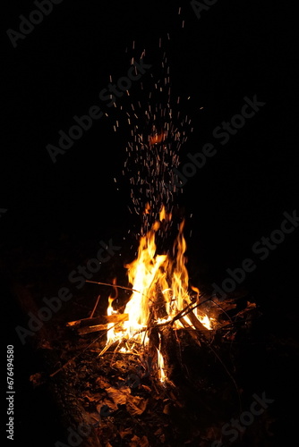 Observe the sparks floating into the night sky from a warm camp fire with red coals 