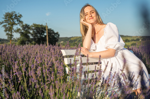 portrait of a relaxed young girl in a white dress, sitting on a white bench, in thought, breathing fresh air, sitting in a lavender field on a sunny day, looking away, thinking