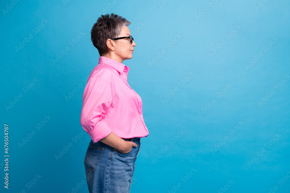 Side profile photo of cool pleasant person with grey hair in eyewear hands in pockets look empty space isolated on blue color background Side profile photo of cool pleasant person with grey hair in eyewear hands in pockets look empty space isolated on blue color background