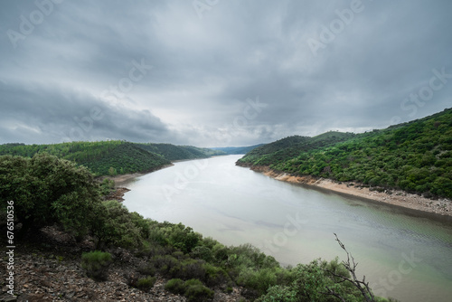 Landscape of a river surrounded by nature and green forest in autumn, a cloudy and rainy day. © Rafael Alejandro