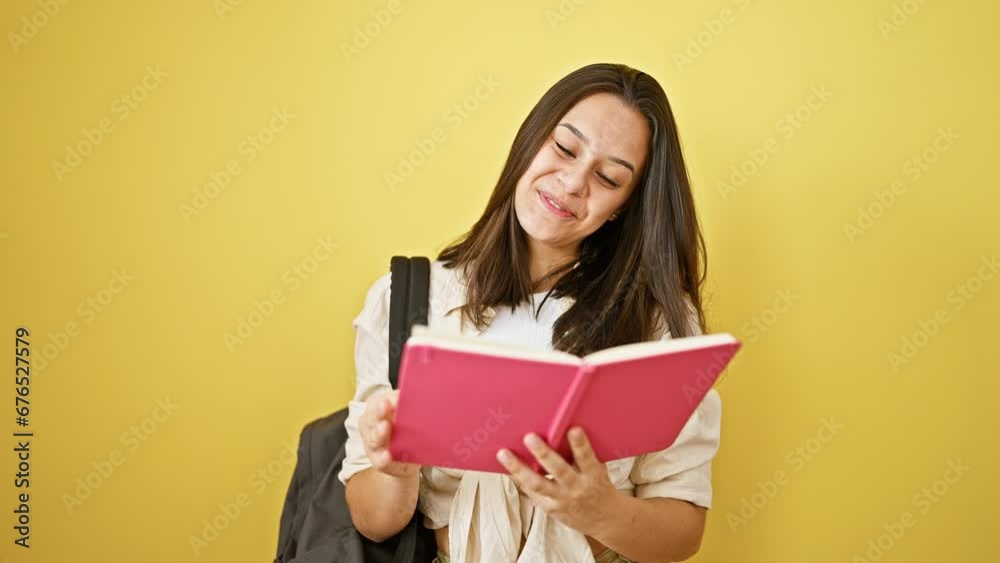 Joyful young hispanic woman with beautiful hairstyle standing confident, cheery, looking cool. casually dressed college student with backpack reading book. isolated on yellow wall background Joyful young hispanic woman with beautiful hairstyle standing confident, cheery, looking cool. casually dressed college student with backpack reading book. isolated on yellow wall background
