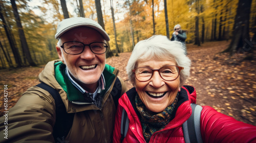 POV portrait of active senior couple looking at camera and smiling while taking selfie photo during hike in autumn forest  copy space