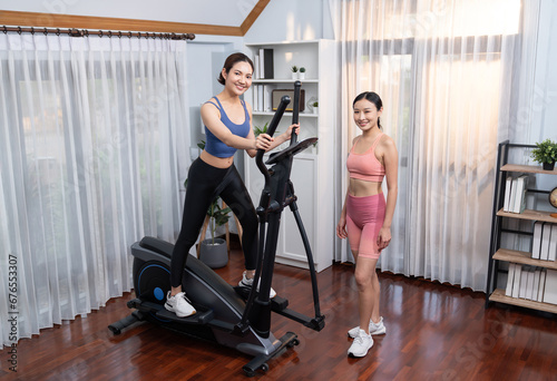 Energetic and strong athletic asian woman running on elliptical running machine at home with workout buddy or trainer. Pursuit of fit physique and commitment to healthy lifestyle. Vigorous