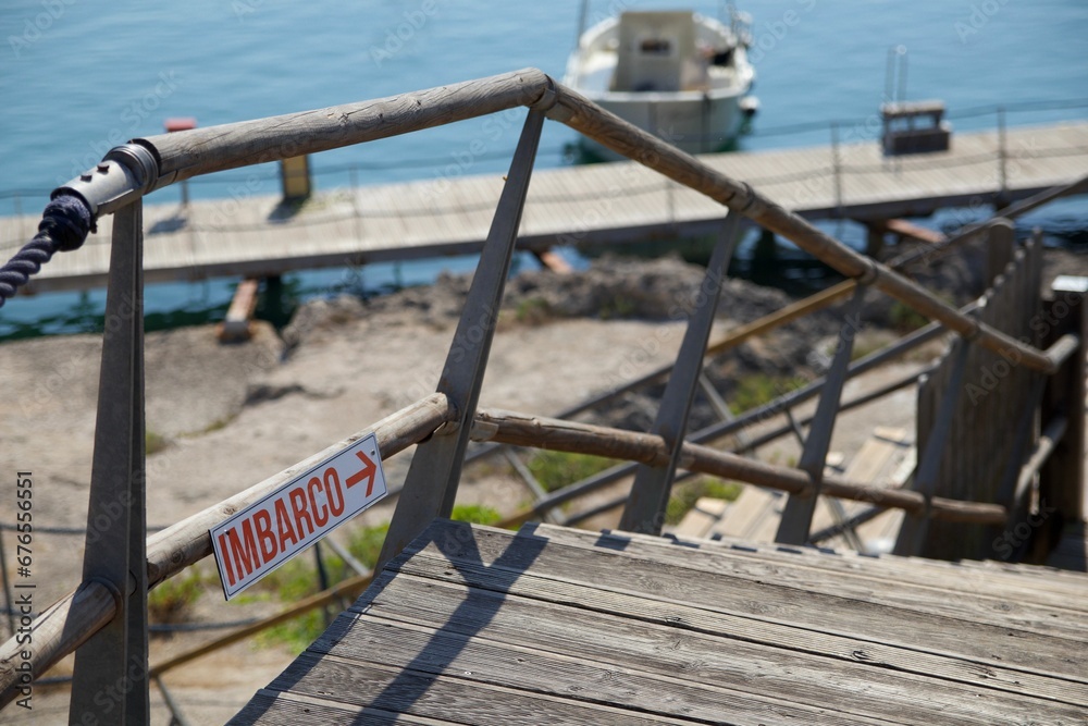 Closeup of Italian boarding sign with direction arrow on the fence of wooden staircase near the sea Closeup of Italian boarding sign with direction arrow on the fence of wooden staircase near the sea