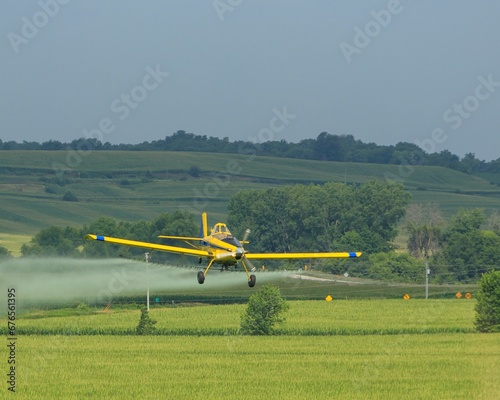 Yellow crop duster flying low while spraying a field