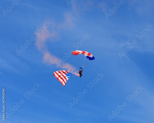 Parachutist descending with the American flag and red smoke attached to his legs