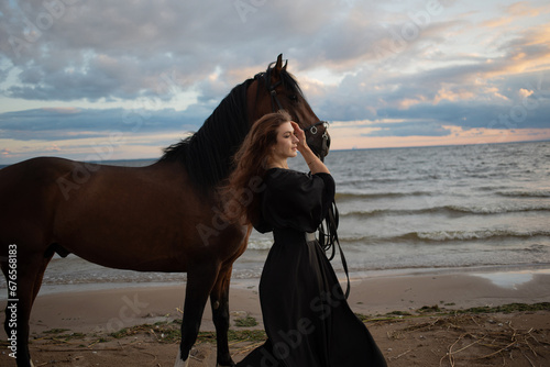 beautiful young rider in a dress and with her hair down, leads her horse along the beach. horseback riding in the open air