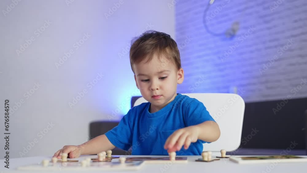 Adorable little toddler in blue t-shirt playing peacefully at the desk. Baby boy matching puzzle pieces. Blurred backdrop. Adorable little toddler in blue t-shirt playing peacefully at the desk. Baby boy matching puzzle pieces. Blurred backdrop.