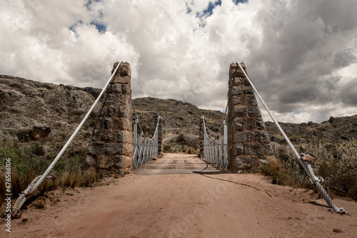 Antiguo puente colgante sobre arroyo serrano en Pampa de Achala, Córdoba, Argentina con cielo nublado