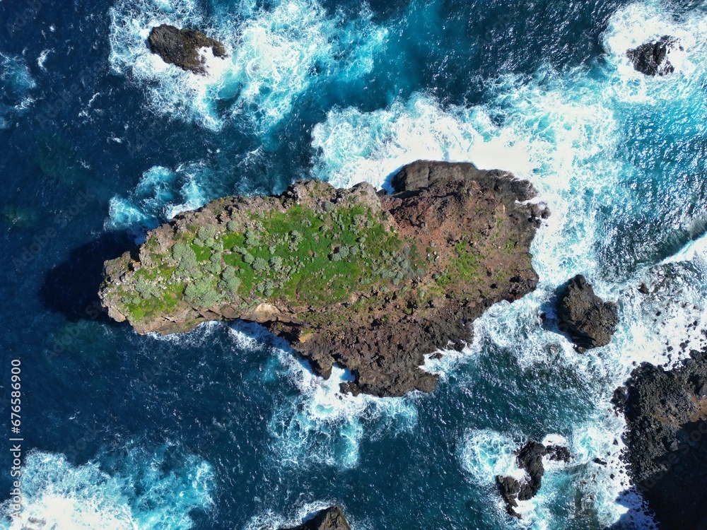 Mała, skalista zielona wyspa na oceanie, obmywana falami. A small, rocky green island in the ocean, washed by the waves. - obrazy, fototapety, plakaty 