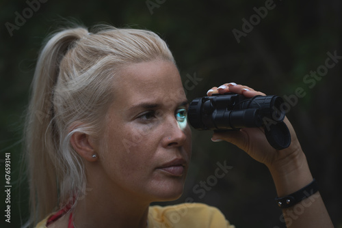 A girl looks through a night vision device at dusk in the forest.
