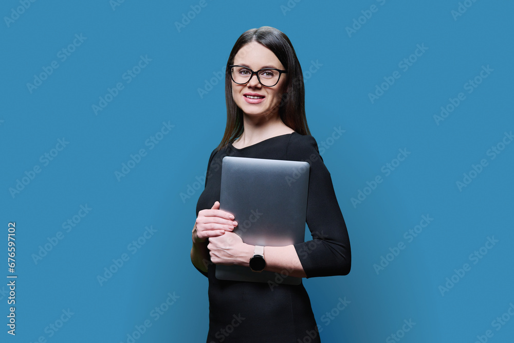 Portrait of young business woman holding laptop, on blue background