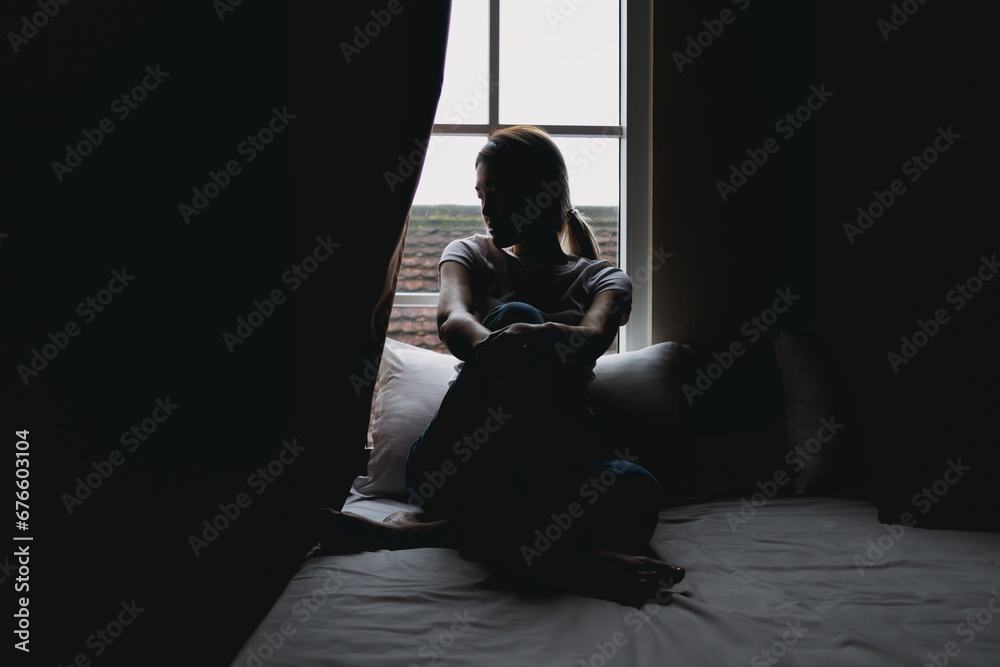 Lonely single asian woman sit alone in dark bedroom with light from curtain.