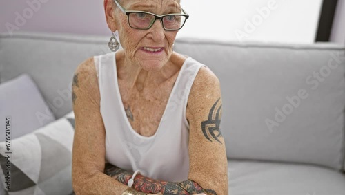 Heartbreaking sight of senior grey-haired woman, sitting solo on sofa at her apartment, suffering from unbearable elbow pain, bone ache hinting at osteoarthritis issue indoors. photo