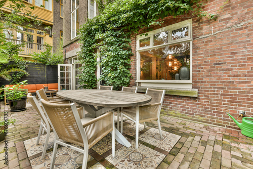 a patio with chairs, table and pots on the brick floor in front of an apartment building that is surrounded by green plants
