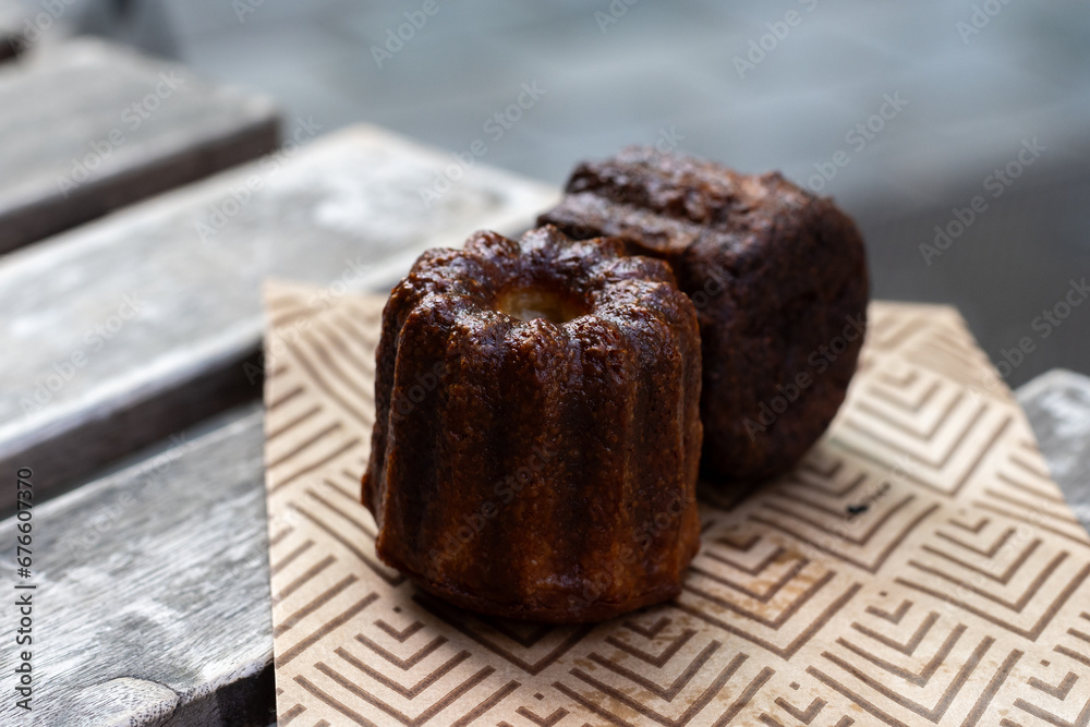 Canele, French pastry flavored with rum and vanilla, soft and tender custard center and dark, caramelized crust specialty of Bordeaux region, France, streets of Bordeaux on background Canele, French pastry flavored with rum and vanilla, soft and tender custard center and dark, caramelized crust specialty of Bordeaux region, France, streets of Bordeaux on background