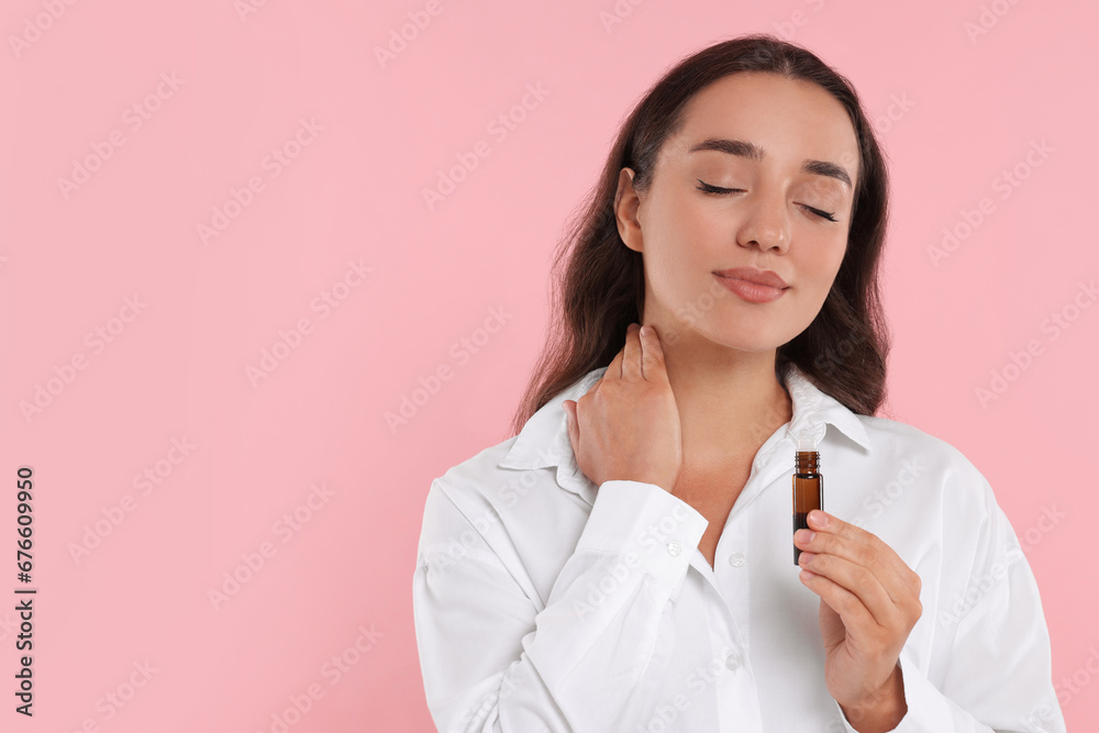 Beautiful young woman with bottle of essential oil on pink background, space for text Beautiful young woman with bottle of essential oil on pink background, space for text
