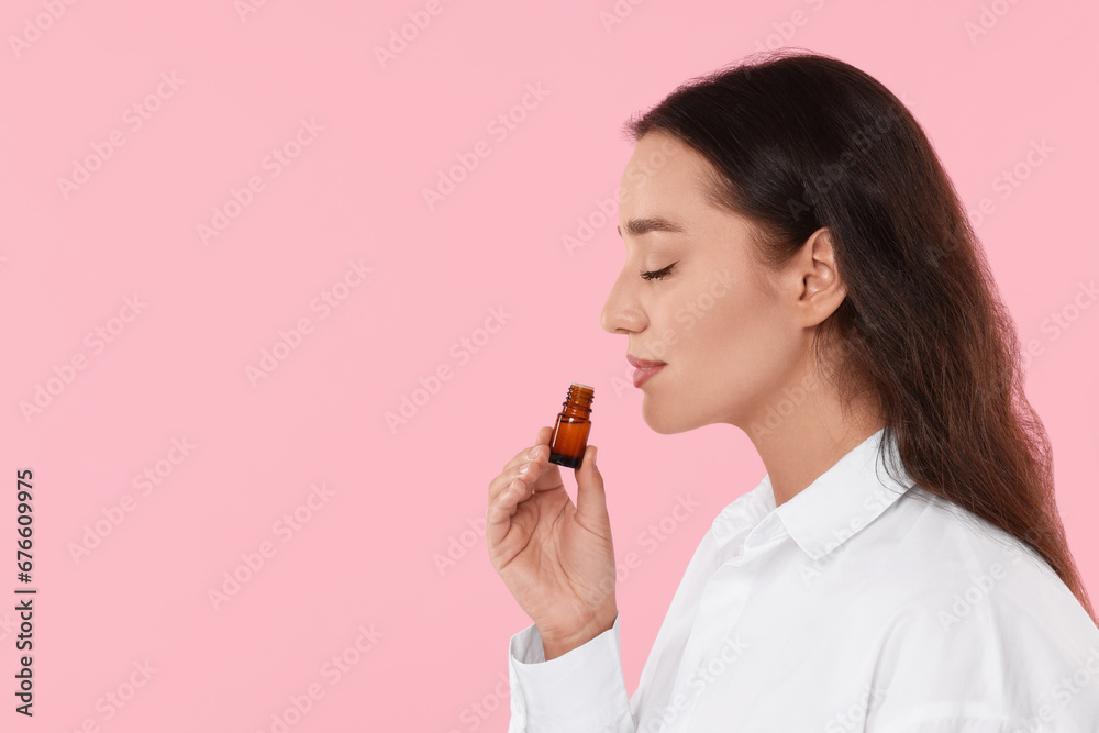 Beautiful young woman with bottle of essential oil on pink background, space for text Beautiful young woman with bottle of essential oil on pink background, space for text