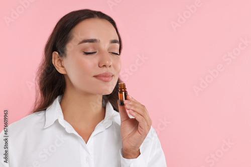 Beautiful young woman with bottle of essential oil on pink background, space for text