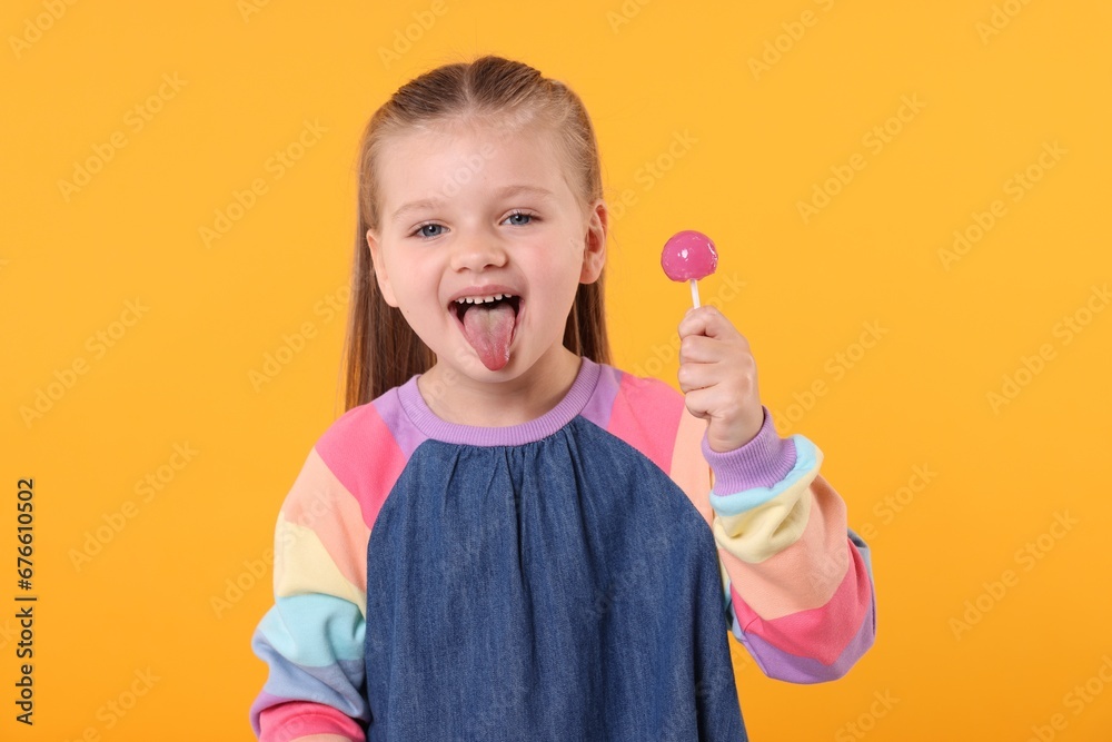 Little girl with lollipop showing tongue on orange background Little girl with lollipop showing tongue on orange background