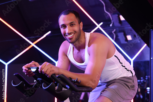 Young man training on exercise bike in fitness club © New Africa