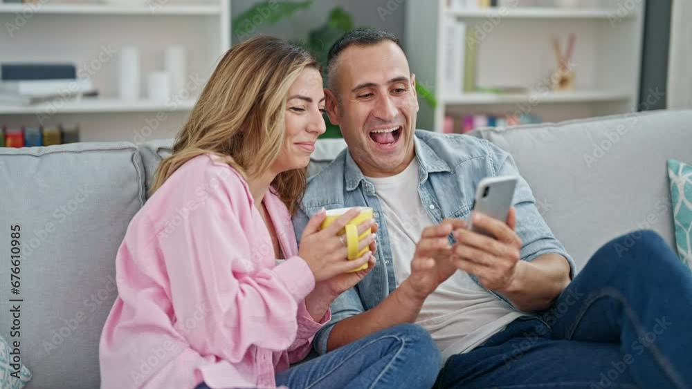 Man and woman couple drinking coffee using smartphone sitting on sofa at home Man and woman couple drinking coffee using smartphone sitting on sofa at home