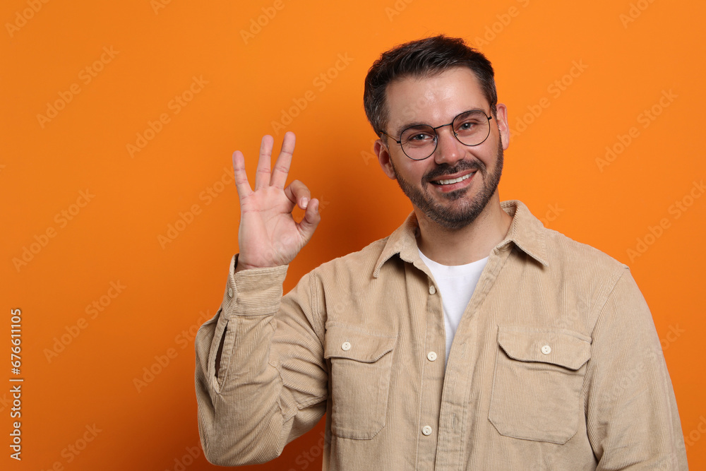 Portrait of smiling man in stylish glasses showing OK gesture on orange background. Space for text Portrait of smiling man in stylish glasses showing OK gesture on orange background. Space for text