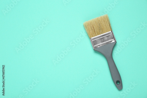 One paint brush with grey handle on turquoise background, top view. Space for text