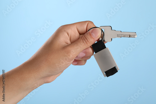 Woman holding key with keychain on light blue background, closeup